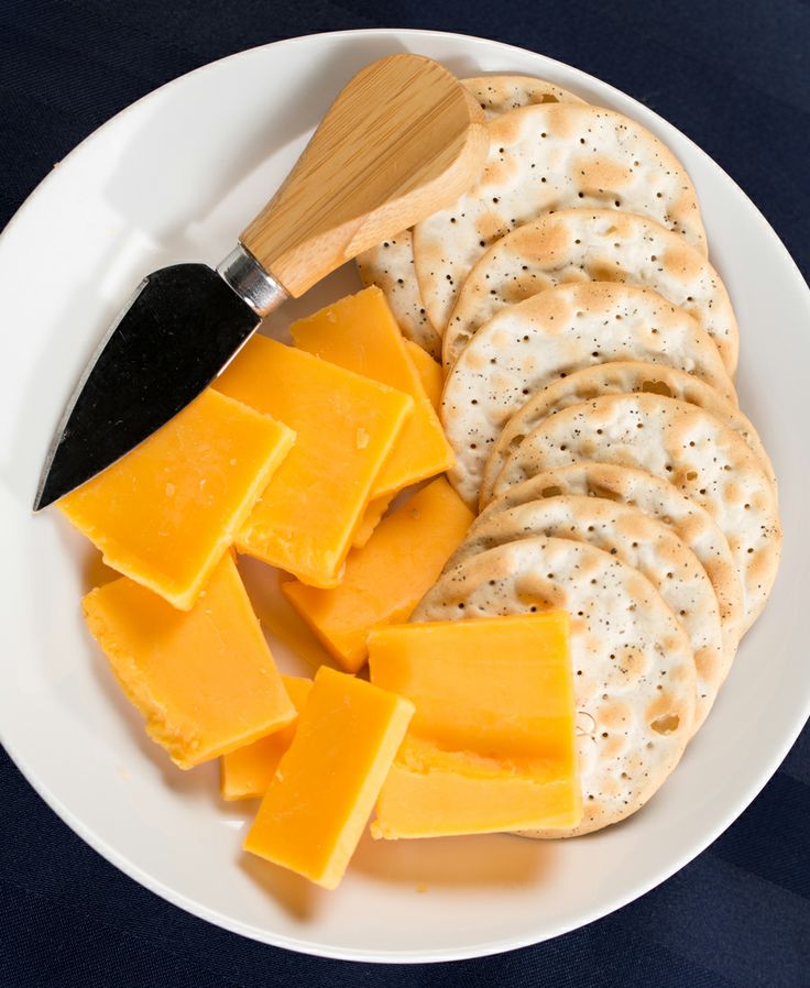 a white plate topped with crackers and cheese next to a wooden spatula on top of a table