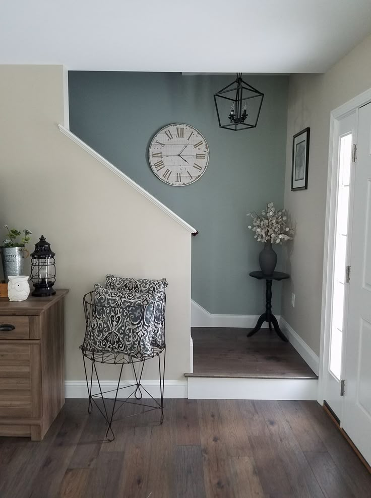 a clock on the wall above a chair in a room with wooden floors and stairs