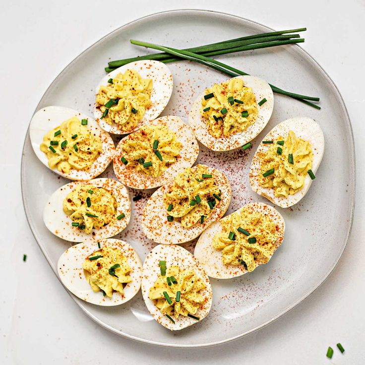 deviled eggs on a white plate with green onions