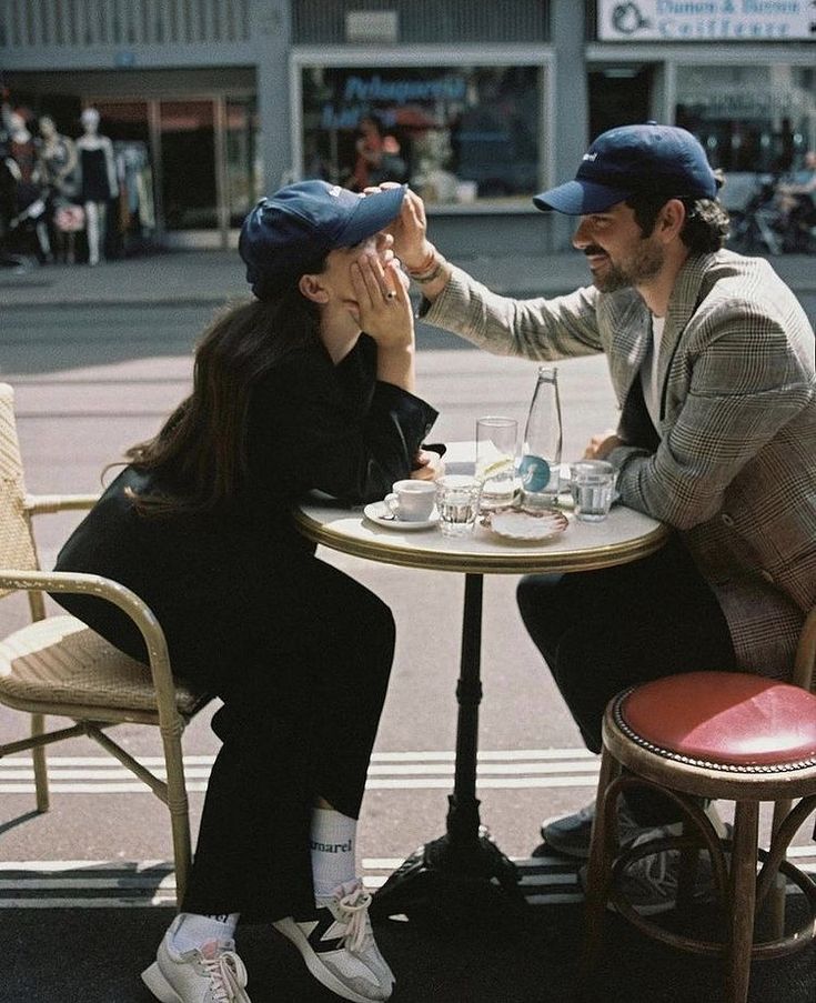 two people sitting at a table with cups and saucers in their hands, one holding the other's hand