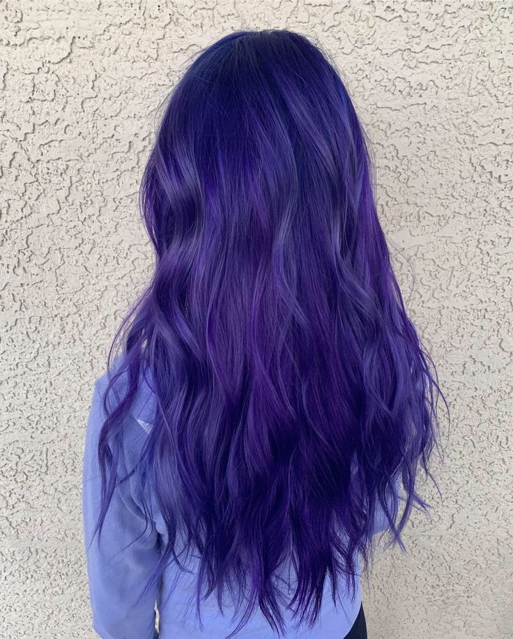 a woman with long purple hair standing in front of a white wall wearing a blue shirt