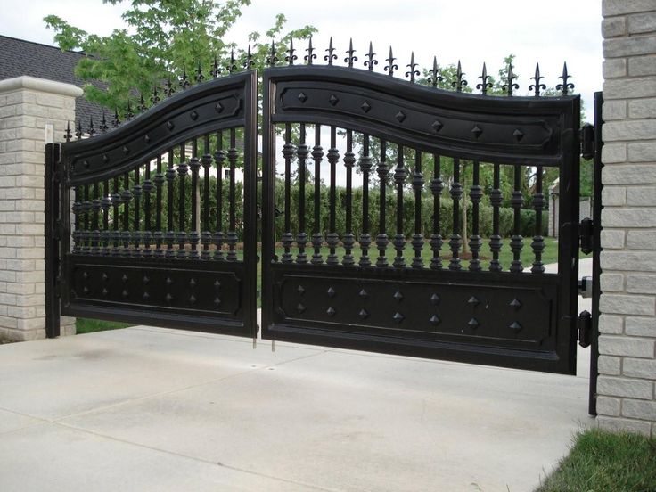 an iron gate is shown in front of a brick wall and tree lined driveway area