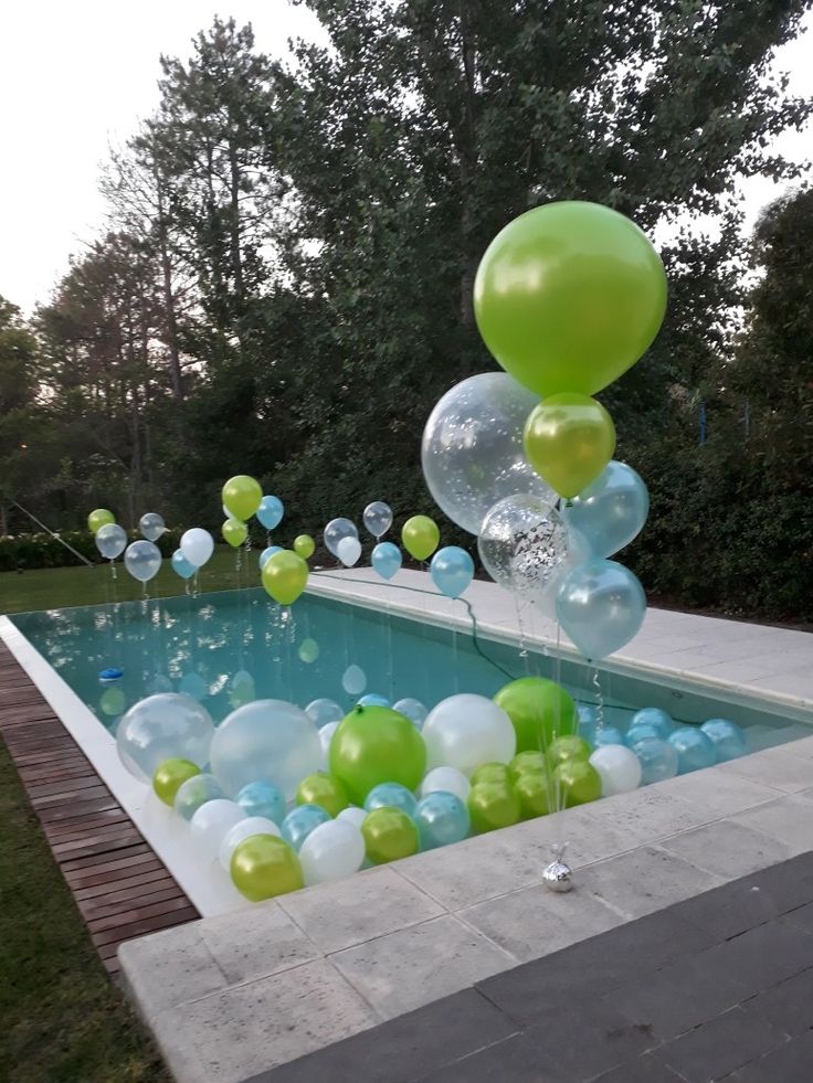 balloons are floating in the air near a swimming pool with green, white and blue balls