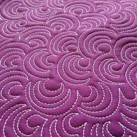 a purple quilt with white stitching on the edge and an intricate design in the middle