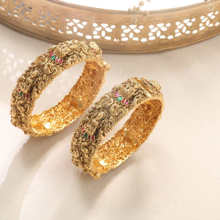 Description: This set of Nakshi work bangles features the divine Goddess Lakshmi, beautifully depicted with intricate craftsmanship. A hint of color is elegantly introduced through the jadau work on the lotus, adding a vibrant touch to the classic design. The combination of traditional artistry and subtle color highlights creates a refined and exquisite piece, perfect for adding a touch of grace to your traditional attire. Product Information: Materials used: 925 Silver with Antique Gold Plating Elegant Zari Work Jewelry For Puja, Gold Traditional Wear With Intricate Design For Navratri, Traditional Gold-plated Openable Jewelry, Elegant Cutdana Bracelets For Navratri, Temple Jewelry For Festivals With Openable Feature, Elegant Beaded Bracelets For Navratri, Elegant Festive Bangle With Zari Work, Festive Temple Jewelry With Openable Details, Elegant Zari Work Bangle For Festive Occasions