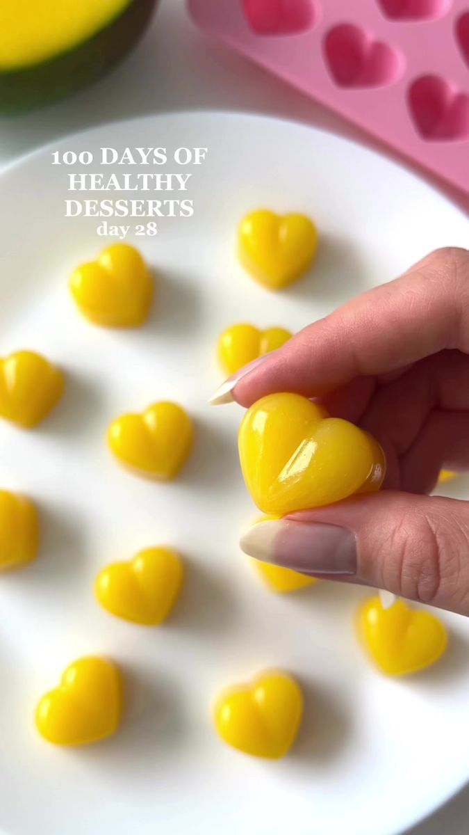 a person holding a yellow heart shaped candy in front of some hearts on a white plate