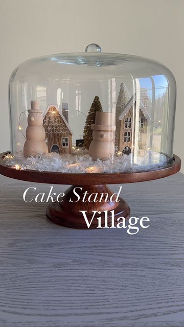 a cake stand with houses under a glass dome on a wooden base and snow around it