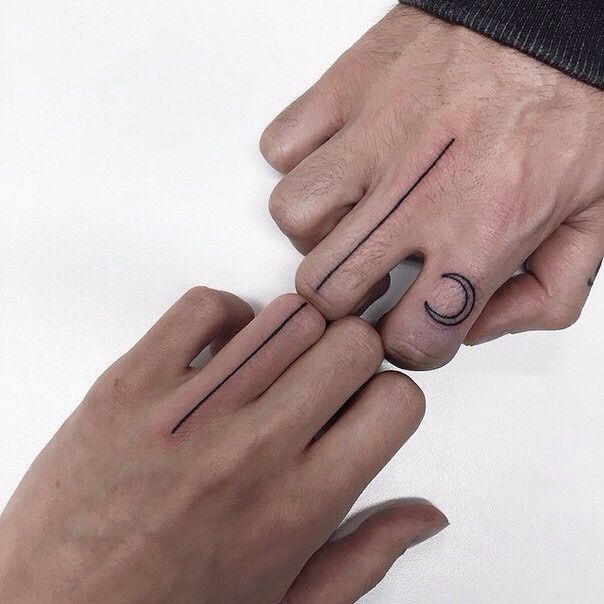 two hands holding each other with small tattoos on their fingers and one has a crescent