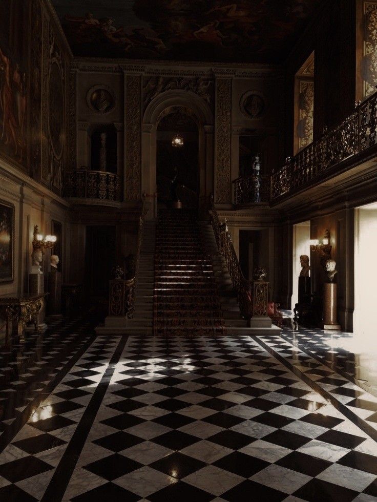 an ornate hallway with black and white checkered flooring, chandelier and staircase