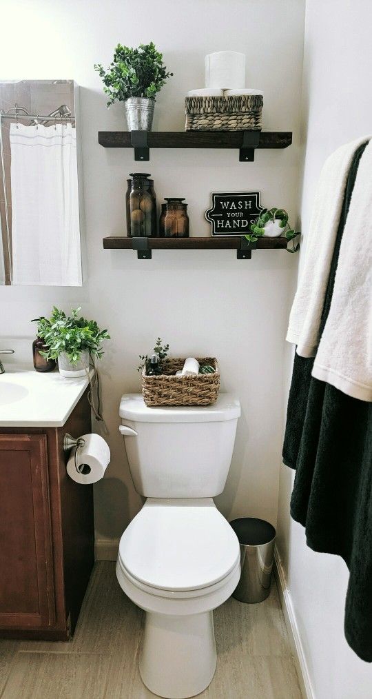 a white toilet sitting in a bathroom next to a wooden cabinet and shelf filled with potted plants