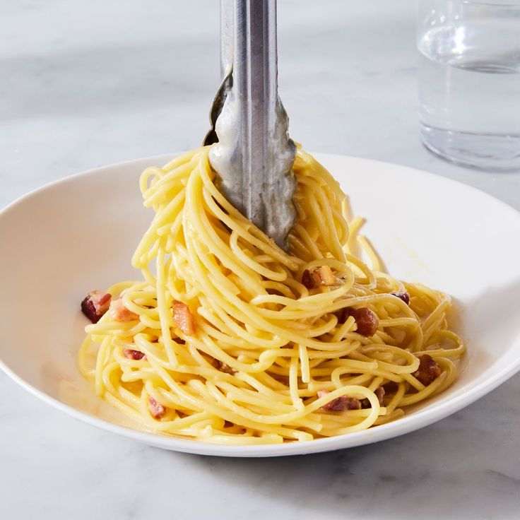 a fork is being used to stir spaghetti in a white bowl on a marble table