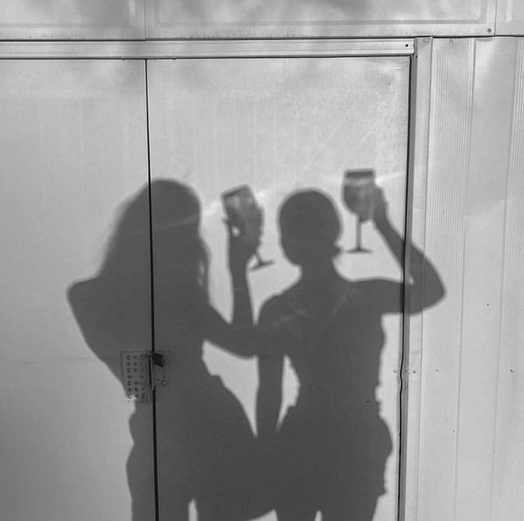 two people standing next to each other holding wine glasses in front of a white wall