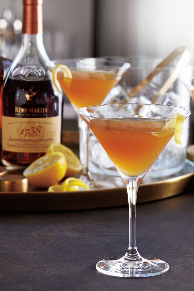 two martini glasses filled with orange juice and garnished with lemons on a tray