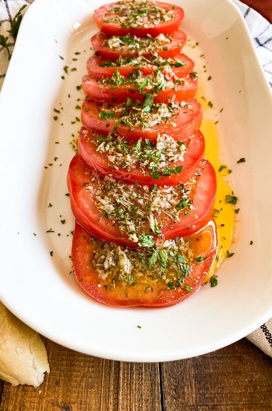 a white plate topped with sliced tomatoes and herbs