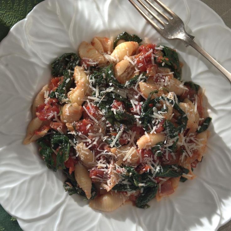 a white plate topped with pasta and spinach covered in parmesan cheese next to a fork