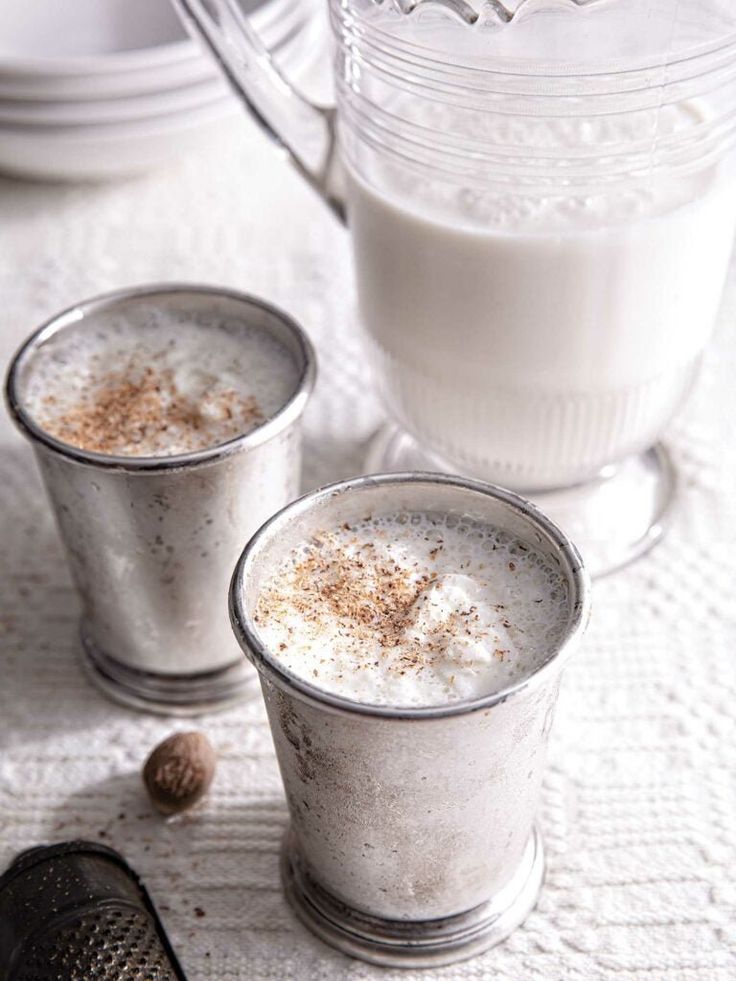 two glasses filled with liquid sitting on top of a table next to a pitcher and spoon