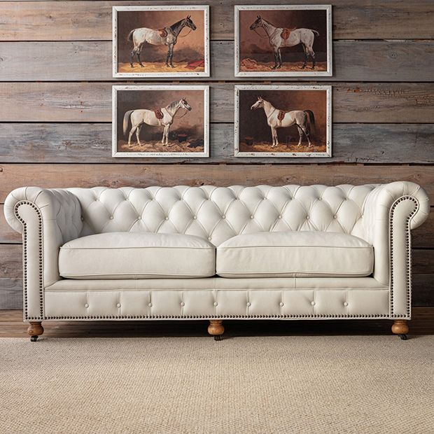 a white leather couch sitting in front of two pictures on the wall above it,