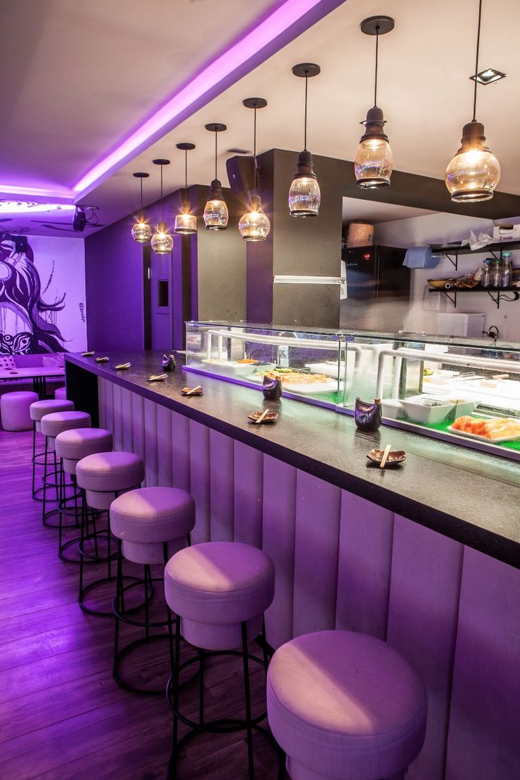 a restaurant with purple lighting and stools in front of the counter area, along with an assortment of food items