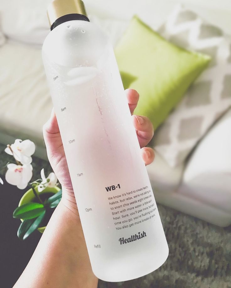 a person holding a water bottle in their hand with flowers on the bed behind it