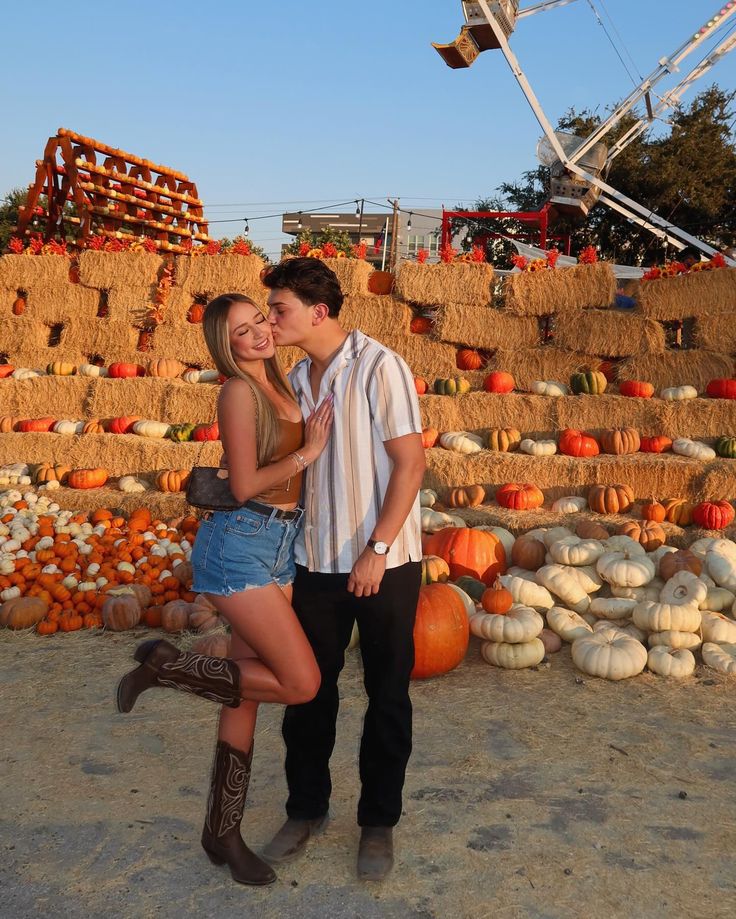 a man and woman standing next to each other in front of hay bales with pumpkins