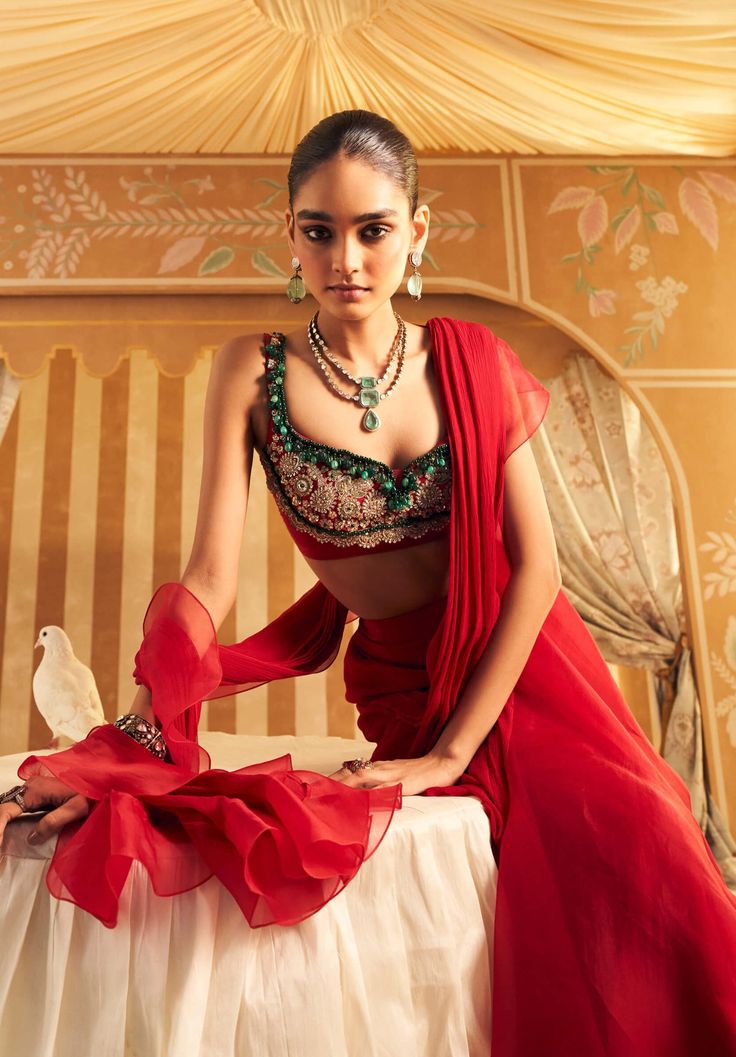 Make a striking impression with the red net embroidered sleeveless blouse, paired with a chiffon drape sari and organza ruffle. The sleeveless blouse showcases intricate red net embroidery, exuding elegance and sophistication. The chiffon sari drapes beautifully, complementing the blouse with a fluid, graceful silhouette. The organza ruffle adds a contemporary twist, creating a stunning fusion of classic and modern elements perfect for any special event. Elegant Red Saree With Ruffles, Luxury Red Embellished Pre-draped Saree, Designer Red Pre-draped Saree With Ruffles, Party-ready Red Ruffled Pre-draped Saree, Red Ruffle Saree, Ruffled Saree, Ridhi Mehra, Ruffle Saree, Embroidered Crop Tops