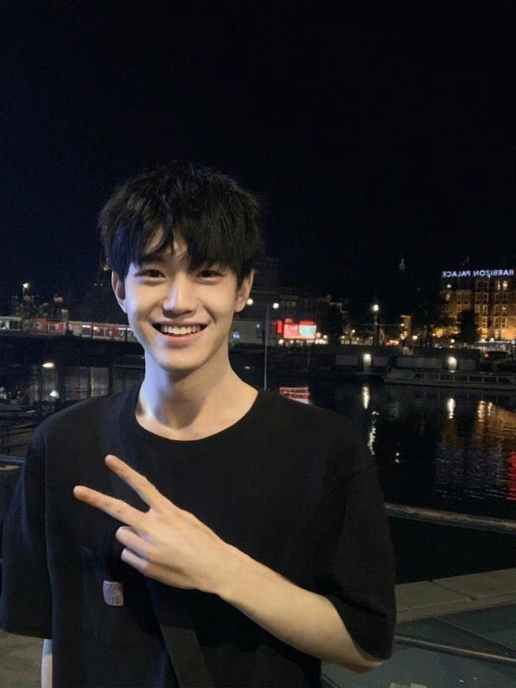 a young man standing next to a body of water at night with his hands together