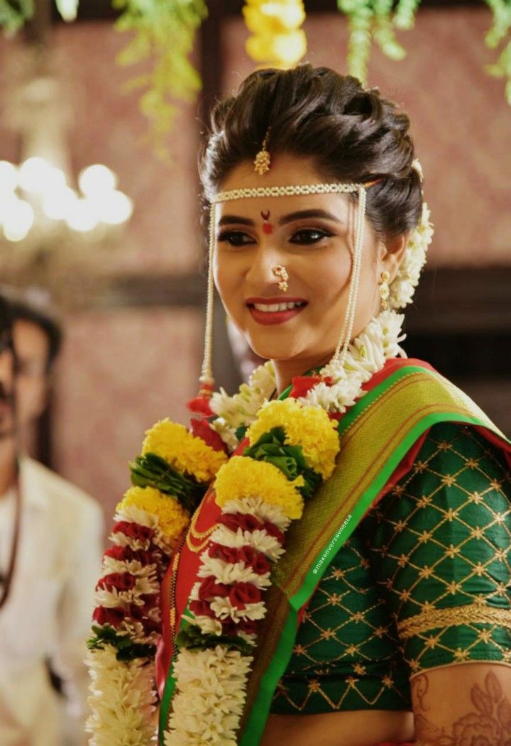 a woman in a green and yellow sari with flowers on her head, smiling at the camera