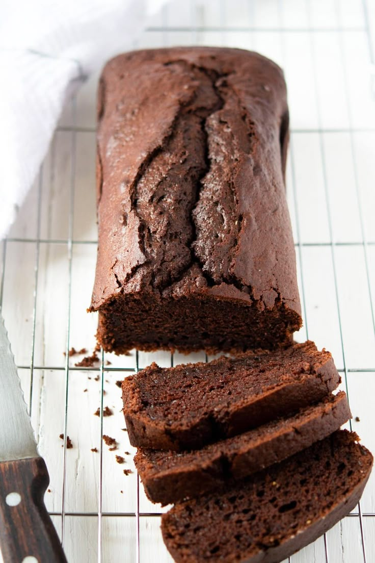 a loaf of chocolate cake sitting on top of a cooling rack next to a knife