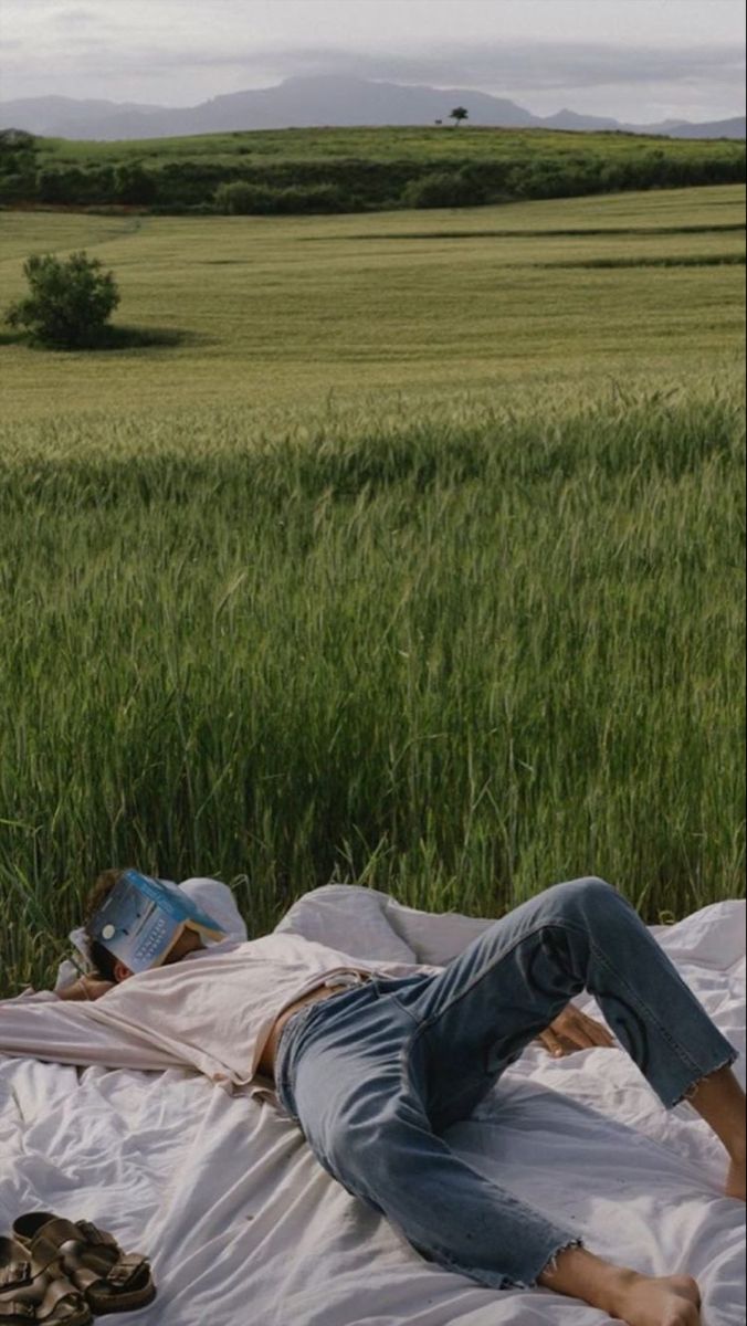 a man laying on top of a bed in a field next to tall green grass