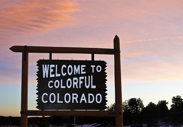 a welcome to colorful colorado sign in front of a pink sky with clouds and trees