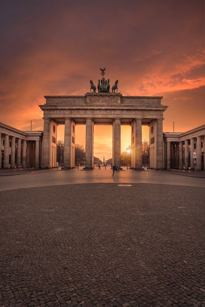 the sun is setting at the end of an arch with statues on top and columns