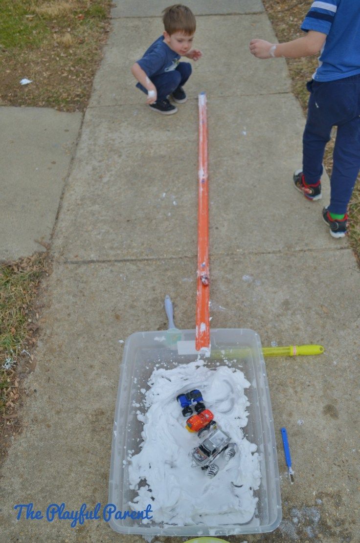 two young boys playing outside in the snow with an orange and white plastic container filled with toys