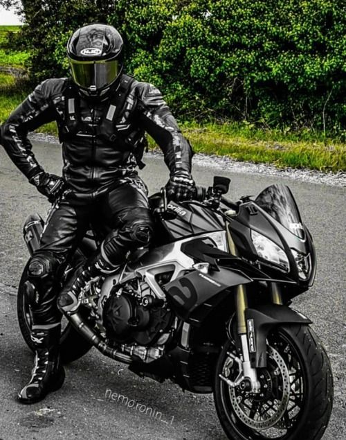 a man sitting on top of a motorcycle in black leathers and helmet, standing next to it