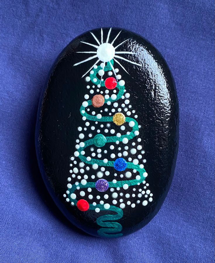 a painted rock with a christmas tree on it's side, sitting on a blue surface