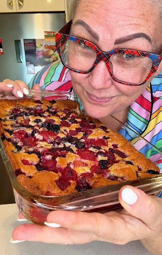 an older woman holding up a pan of fruit cake