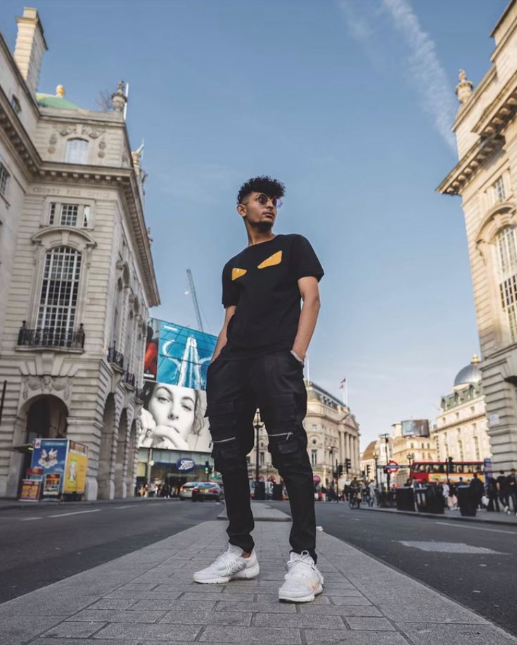 a man standing in the middle of an empty street with buildings and people behind him