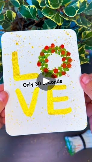 someone holding up a card with the word love on it and a wreath in the middle