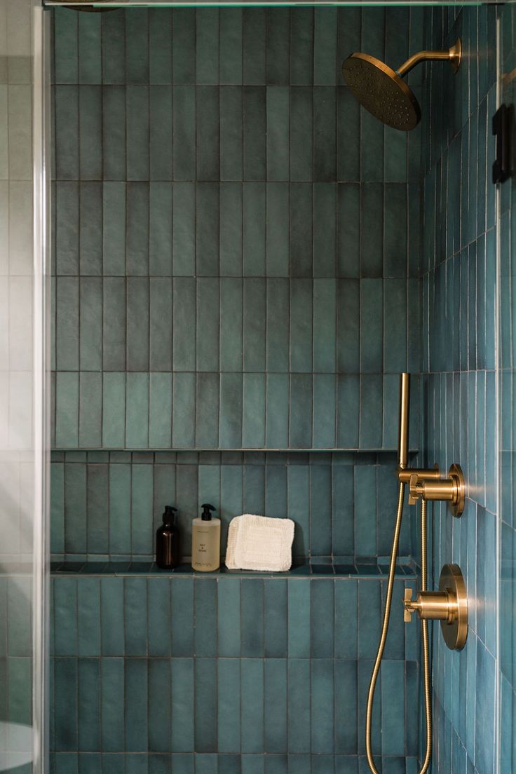 a bathroom with blue tiles and gold fixtures on the shower head, hand held by two brass faucets