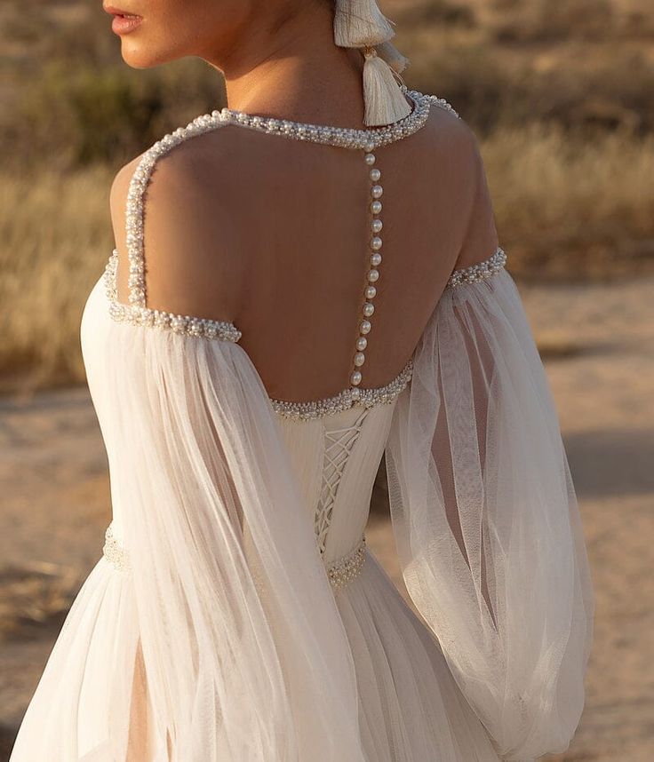 the back of a woman's white dress with pearls on her neck and shoulders