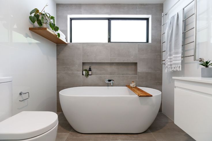 a white bath tub sitting next to a toilet under a window in a bathroom on top of a tiled floor