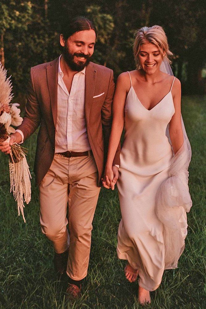 a bride and groom are walking through the grass holding each other's hands as they walk towards the camera