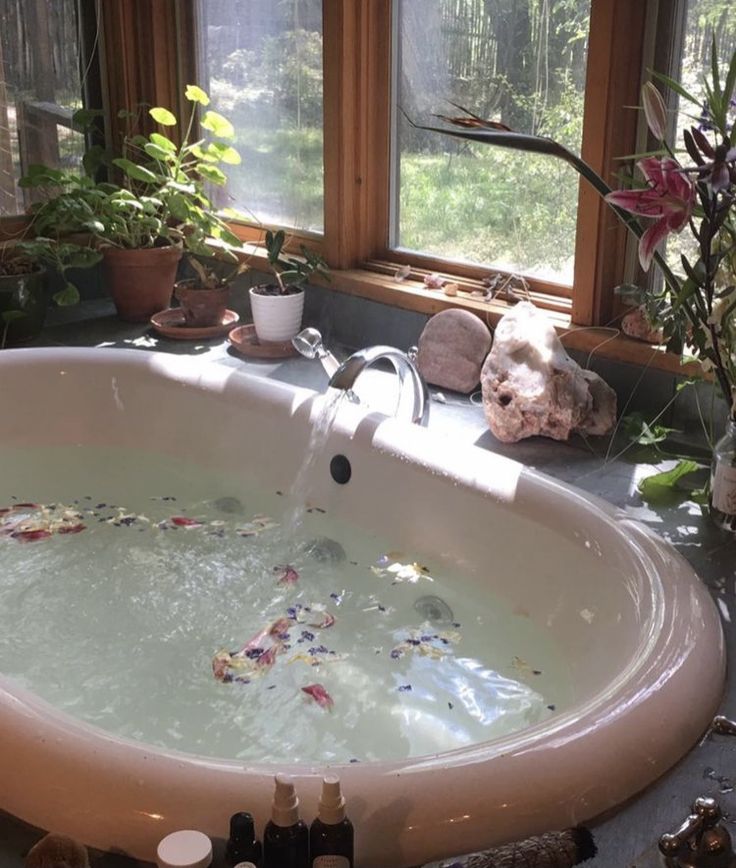 a bathtub filled with lots of water next to plants and bottles on the counter