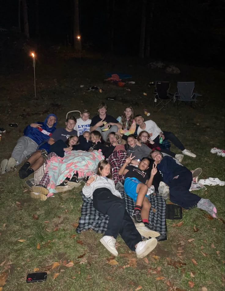 a group of people laying on the ground in the grass at night with their arms around each other