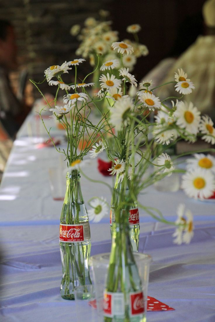 two vases filled with daisies sitting on top of a blue tablecloth covered table