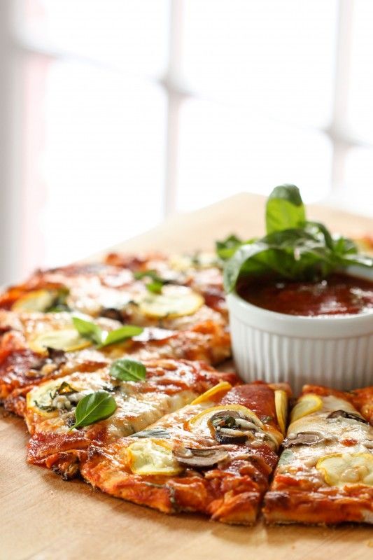 a pizza sitting on top of a wooden cutting board next to a bowl of sauce