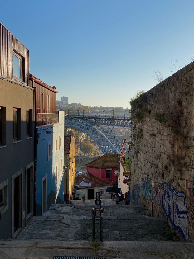 an alley way with graffiti on the walls and buildings in the background, near a bridge