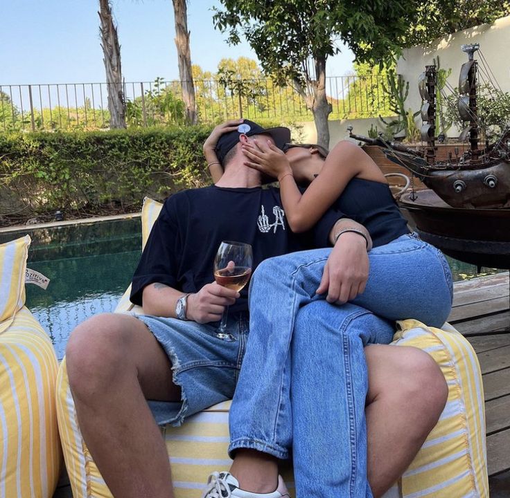 a man and woman sitting next to each other on top of a yellow couch near a pool