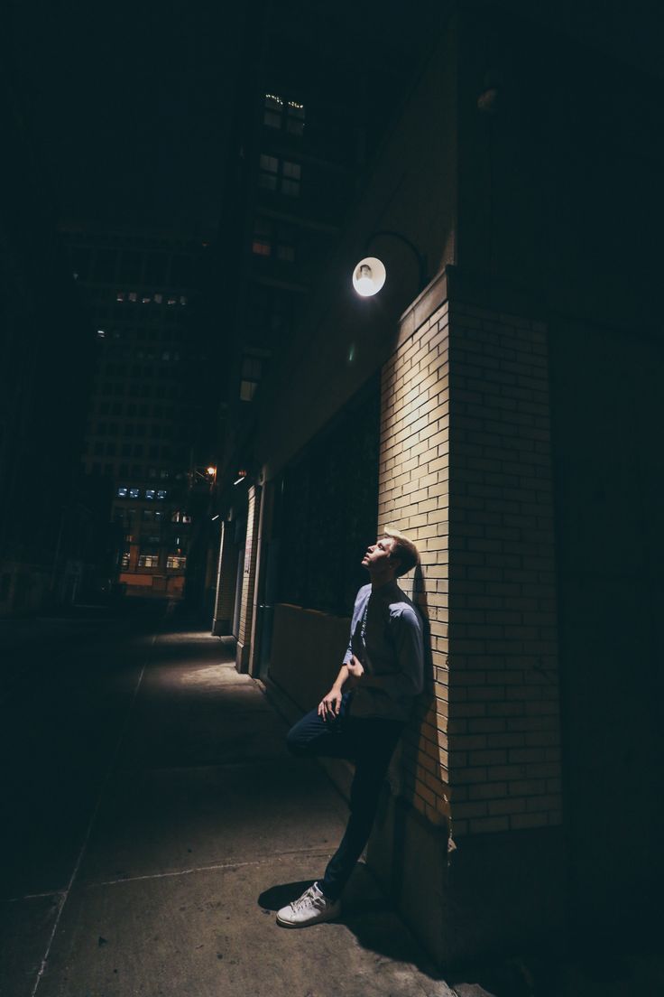 a man sitting on the side of a building at night with his head up and eyes closed