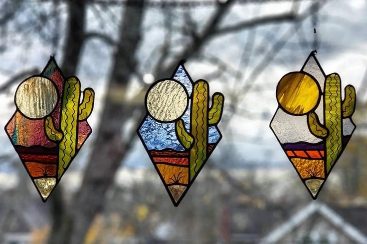 three stained glass windows with cactus designs hanging from the ceiling in front of a tree