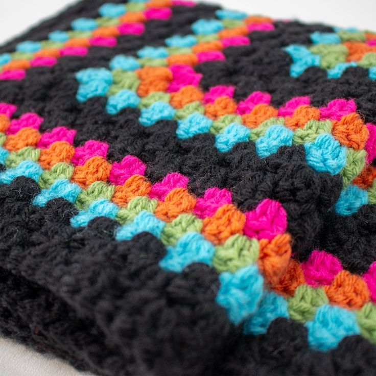 a crocheted blanket is laying on top of a white bed sheet with multicolored squares